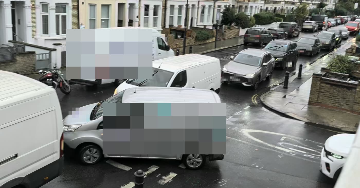 Vans and cars queued across the KEEP CLEAR marking at a side-road junction on a wet day.