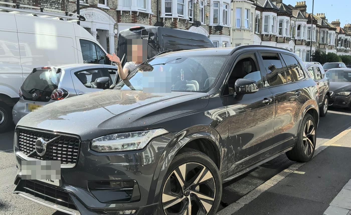 A driver standing at the open door of a dark SUV, gesturing angrily. Face and number plates are pixelated.